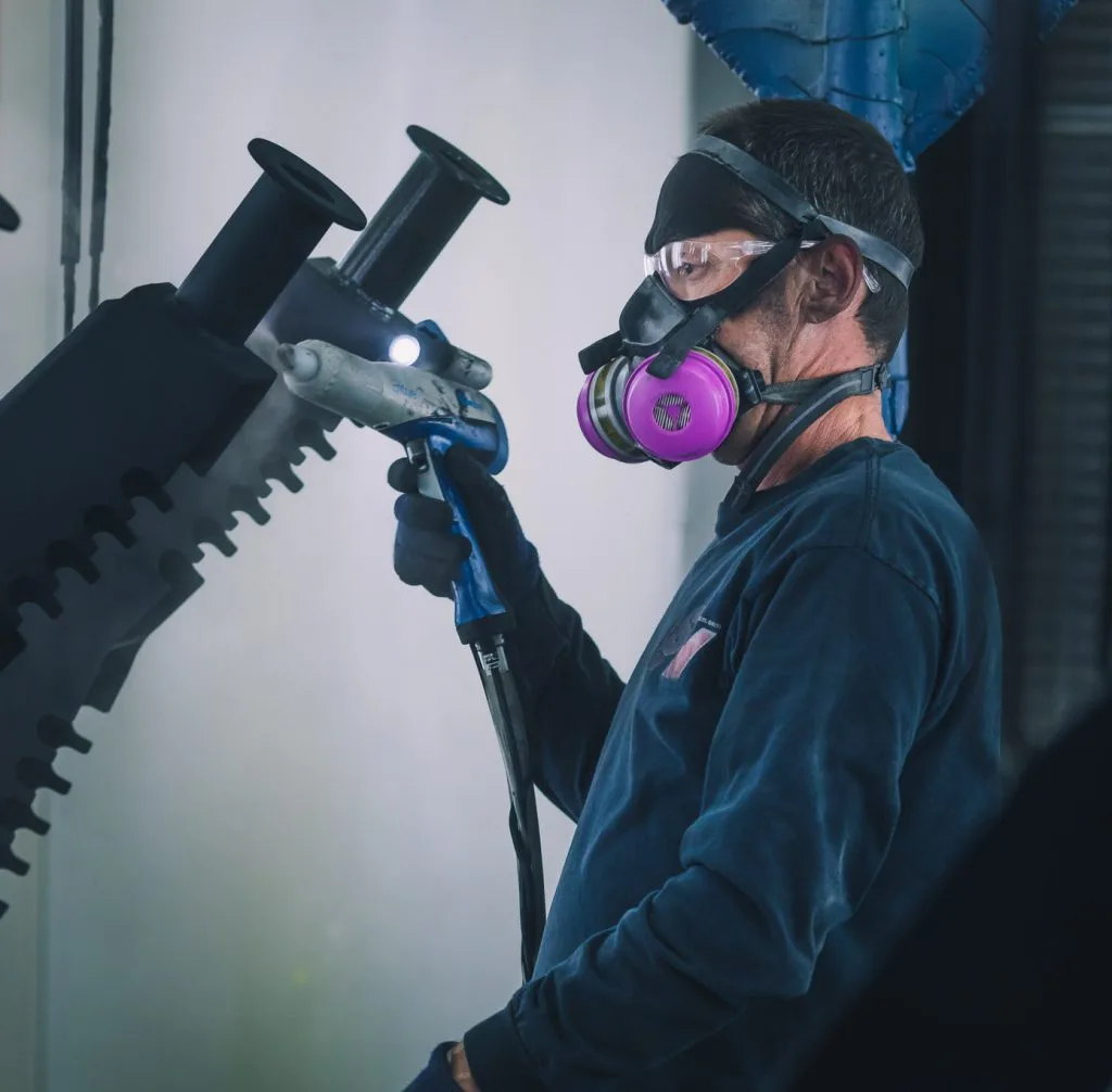LSM technician in a respirator applying powder coating with a spray gun